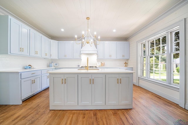 kitchen featuring decorative light fixtures, light hardwood / wood-style floors, and an island with sink