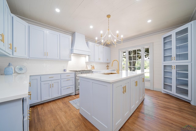 kitchen with pendant lighting, premium range hood, a center island with sink, sink, and high end stainless steel range