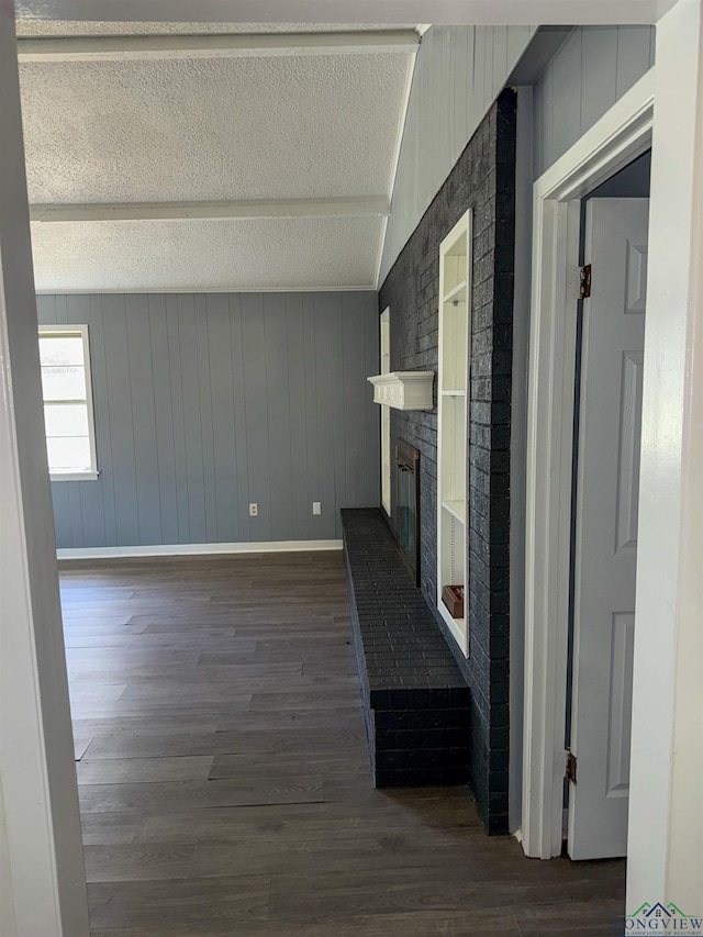 unfurnished living room featuring dark wood-style floors, a brick fireplace, a textured ceiling, and baseboards