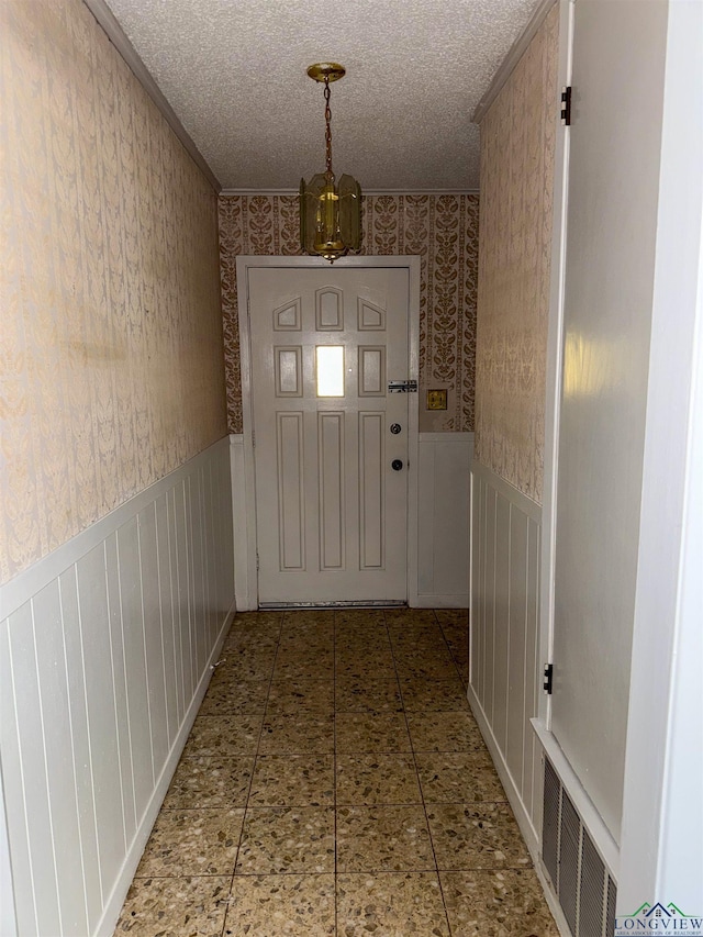 entryway with a textured ceiling, wainscoting, and wallpapered walls