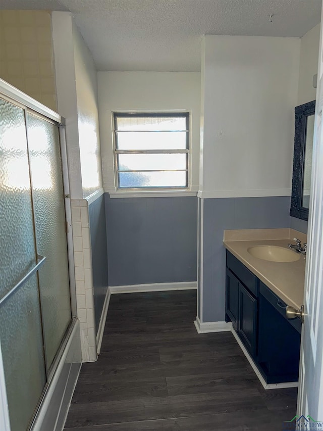 full bathroom featuring a wainscoted wall, a textured ceiling, wood finished floors, combined bath / shower with glass door, and vanity