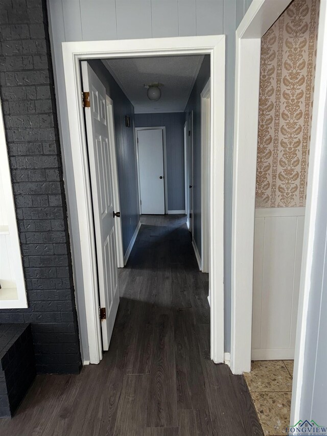 hall featuring dark wood-style floors, a decorative wall, and wainscoting