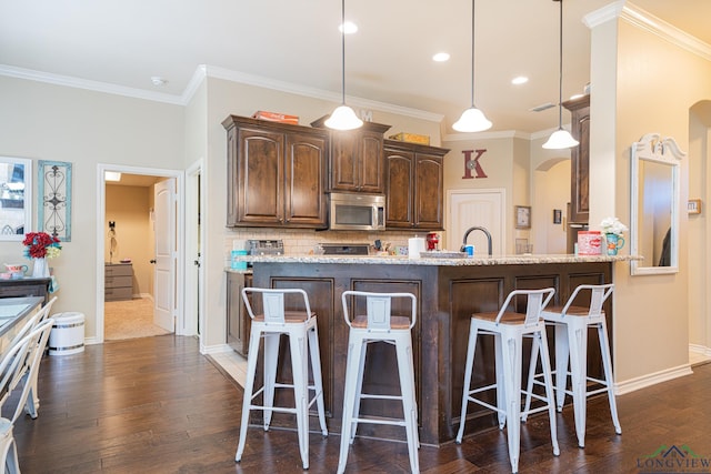 kitchen featuring a kitchen bar, light stone counters, tasteful backsplash, and decorative light fixtures