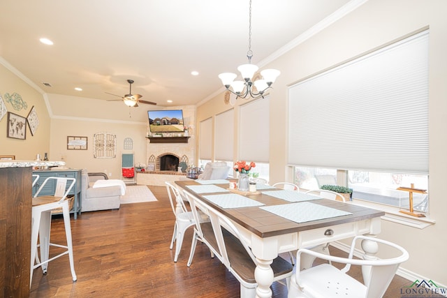 dining room featuring a large fireplace, dark wood-type flooring, ceiling fan with notable chandelier, and ornamental molding