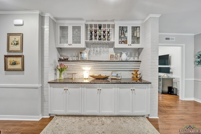 bar featuring wood finished floors, a dry bar, crown molding, and baseboards
