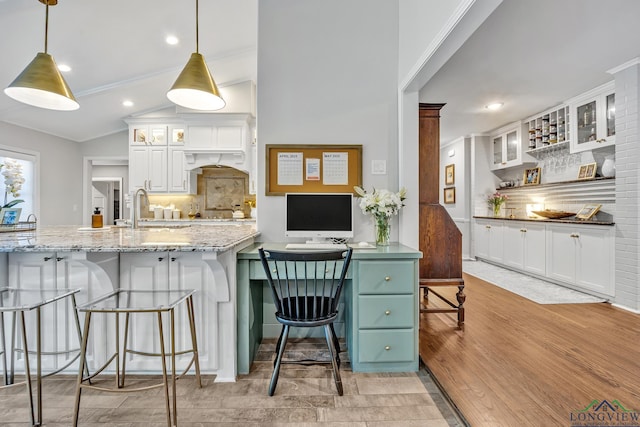 kitchen featuring a sink, white cabinetry, decorative backsplash, light stone counters, and a breakfast bar area