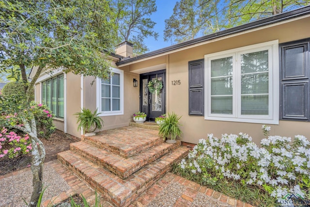 view of exterior entry with a chimney and stucco siding