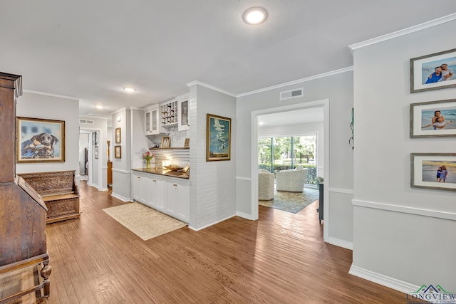hall featuring wood finished floors, visible vents, crown molding, and baseboards