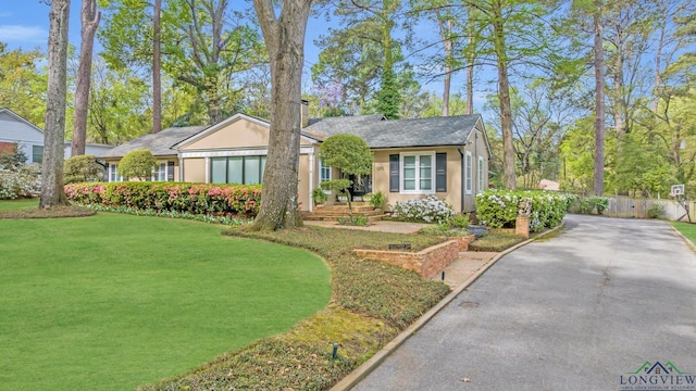 ranch-style home with stucco siding, a front lawn, aphalt driveway, and fence