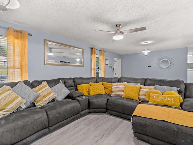 living room featuring ceiling fan, light hardwood / wood-style floors, and a textured ceiling