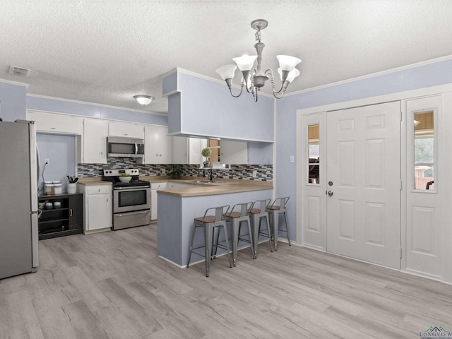 kitchen featuring kitchen peninsula, appliances with stainless steel finishes, crown molding, decorative light fixtures, and white cabinetry