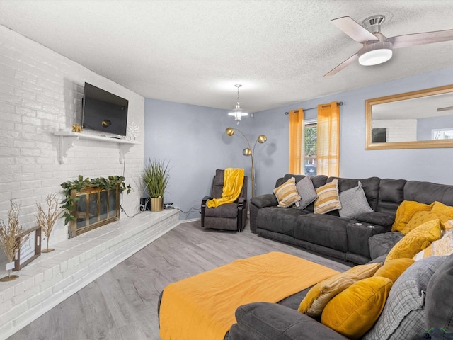 living room featuring ceiling fan, a fireplace, a textured ceiling, and light wood-type flooring