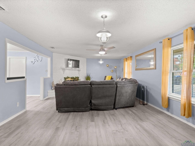 living room with ceiling fan, light wood-type flooring, a textured ceiling, and a brick fireplace