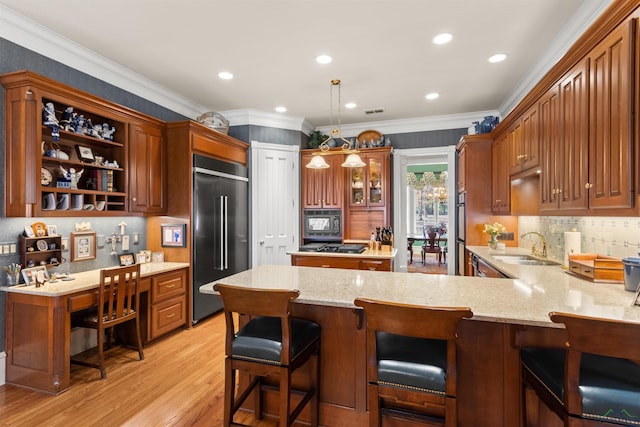 kitchen with a breakfast bar, built in desk, decorative light fixtures, built in appliances, and kitchen peninsula