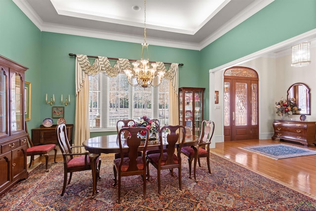 dining space with crown molding, dark wood-type flooring, a notable chandelier, and a tray ceiling