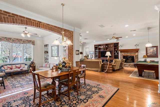 dining space with a stone fireplace, hardwood / wood-style flooring, ornamental molding, pool table, and ceiling fan