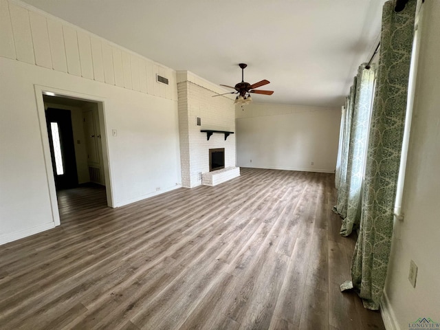 unfurnished living room featuring a brick fireplace, dark wood-type flooring, ceiling fan, and plenty of natural light