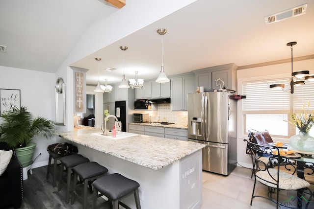 kitchen featuring a breakfast bar area, a peninsula, visible vents, stainless steel refrigerator with ice dispenser, and decorative backsplash