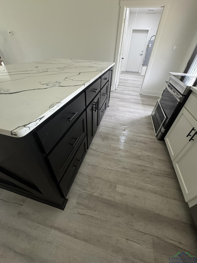 kitchen with light stone countertops, white cabinets, light hardwood / wood-style flooring, and stainless steel electric range oven