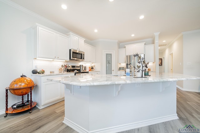 kitchen with a kitchen breakfast bar, a spacious island, light wood-type flooring, appliances with stainless steel finishes, and white cabinetry