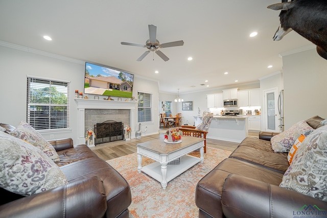 living room with a fireplace, light wood-type flooring, ceiling fan, and crown molding