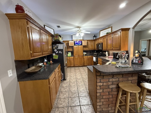 302 Meadowbrook Ln, Ore City, TX 75683 - kitchen featuring appliances with stainless steel finishes, a peninsula, ceiling fan, dark countertops, and a kitchen breakfast bar
