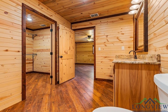 half bathroom with wooden walls, wood finished floors, visible vents, wooden ceiling, and toilet