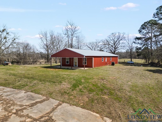 back of property with an outbuilding, cooling unit, metal roof, and a yard