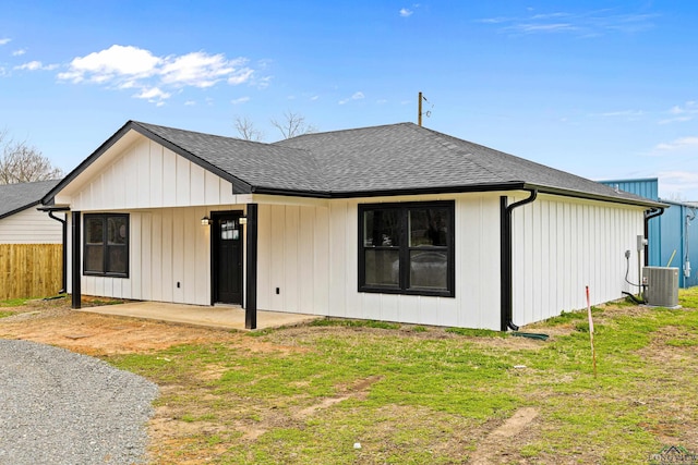 rear view of property with a lawn, a patio, fence, roof with shingles, and central AC unit