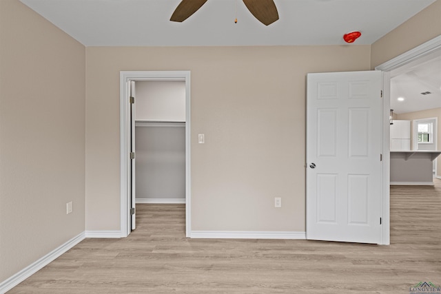 unfurnished bedroom featuring a walk in closet, baseboards, a closet, and light wood finished floors