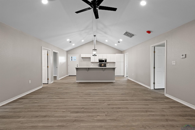 kitchen with stainless steel microwave, open floor plan, a center island with sink, wood finished floors, and white cabinetry