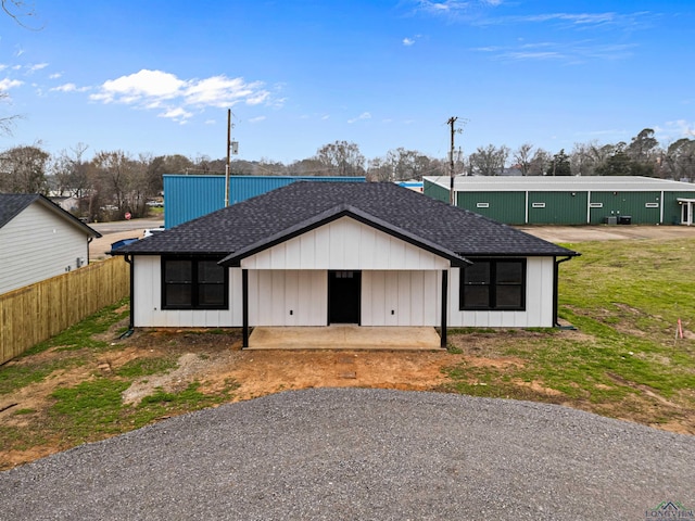 view of front of house featuring a patio area, board and batten siding, roof with shingles, and fence