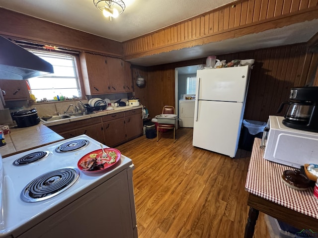 kitchen with white appliances, washer / dryer, a sink, light wood-style floors, and wood walls