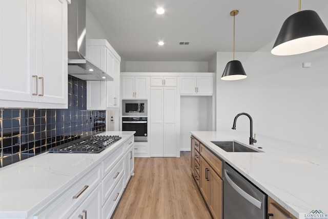 kitchen featuring appliances with stainless steel finishes, wall chimney exhaust hood, sink, pendant lighting, and white cabinetry