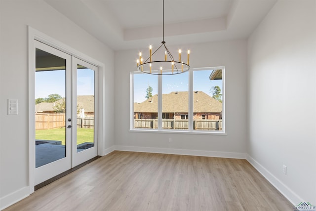 unfurnished dining area featuring a raised ceiling, french doors, light hardwood / wood-style flooring, and an inviting chandelier