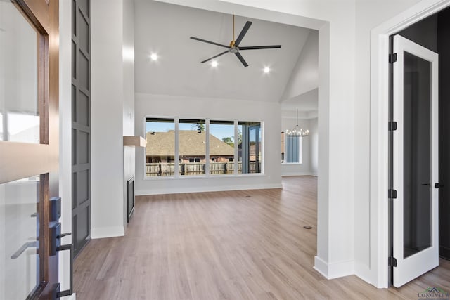 unfurnished living room featuring light hardwood / wood-style flooring, high vaulted ceiling, and ceiling fan with notable chandelier