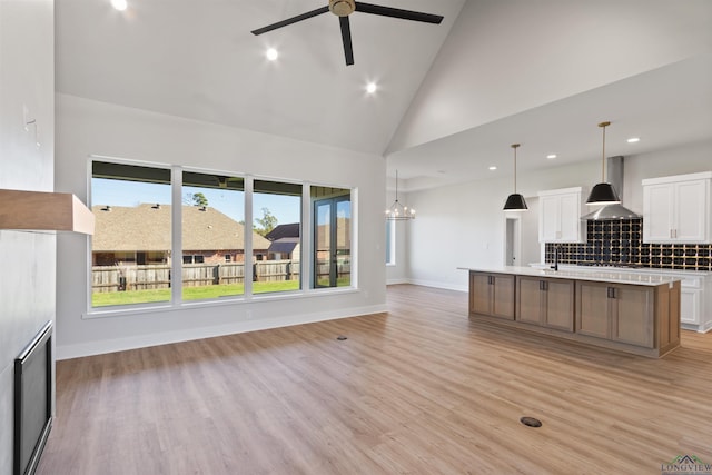 unfurnished living room with ceiling fan with notable chandelier, light hardwood / wood-style flooring, high vaulted ceiling, and sink