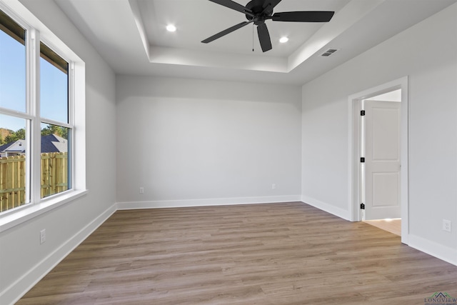 spare room featuring a tray ceiling, ceiling fan, and light hardwood / wood-style floors