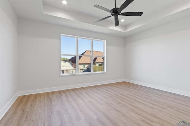 empty room with a raised ceiling, ceiling fan, and light wood-type flooring