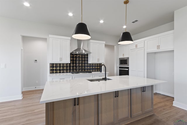 kitchen with wall chimney exhaust hood, a center island with sink, white cabinets, and sink