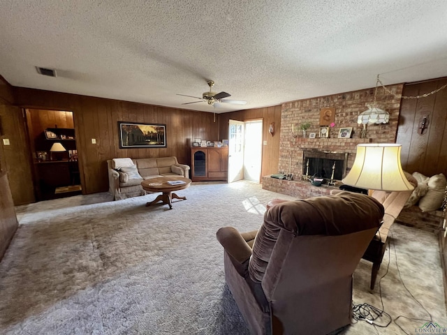 carpeted living room with a textured ceiling, wood walls, ceiling fan, and a fireplace