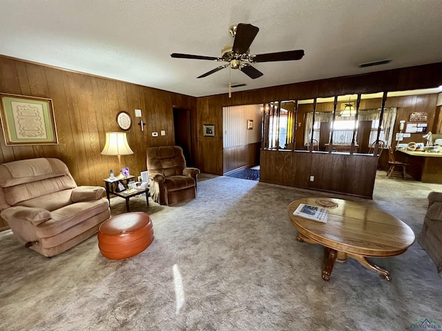 living room with a textured ceiling, ceiling fan, wooden walls, and carpet