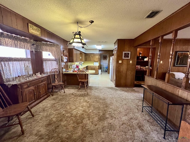 dining room with a textured ceiling, light colored carpet, and wooden walls