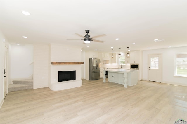 unfurnished living room with ceiling fan, light hardwood / wood-style flooring, sink, and a brick fireplace