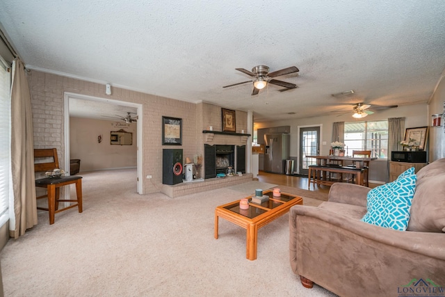 living room featuring ceiling fan, brick wall, carpet floors, a textured ceiling, and a fireplace