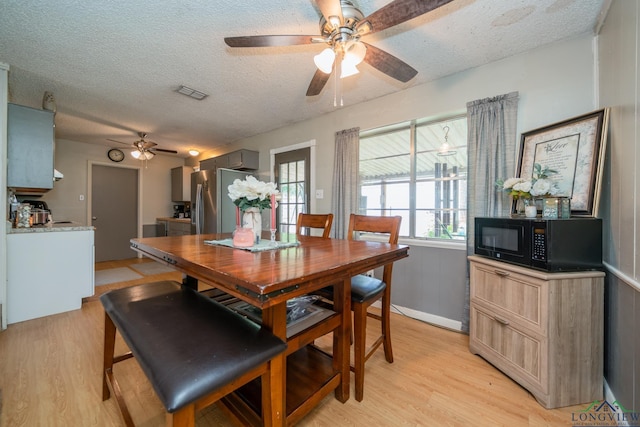 dining space with ceiling fan, light wood-type flooring, and a textured ceiling