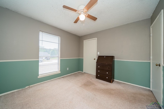 unfurnished bedroom with ceiling fan, light colored carpet, and a textured ceiling