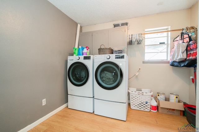 laundry room featuring light hardwood / wood-style flooring, cabinets, a textured ceiling, and washing machine and clothes dryer