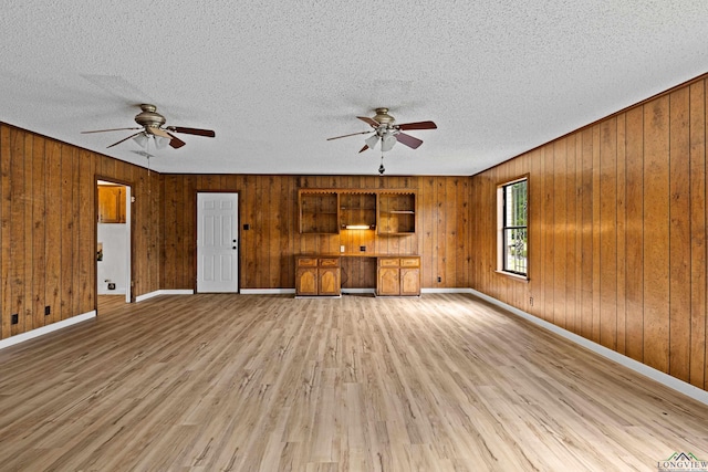 unfurnished living room featuring built in desk, ceiling fan, and wooden walls