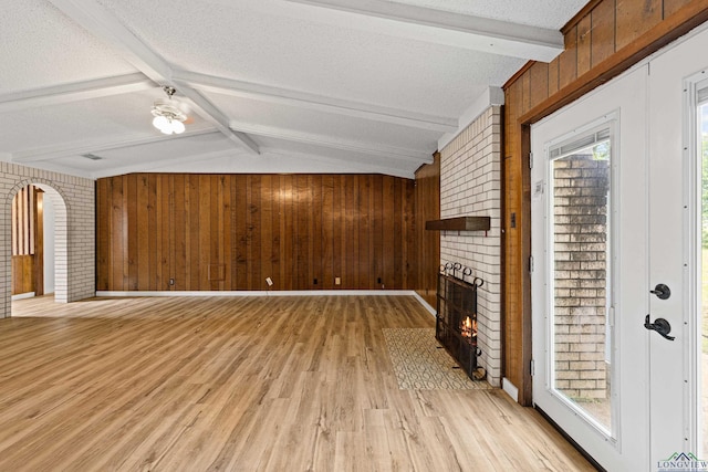 unfurnished living room featuring a textured ceiling, lofted ceiling with beams, a brick fireplace, and wooden walls